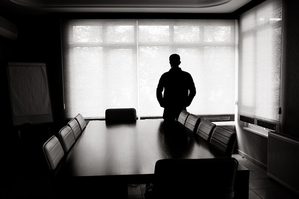 Svartvit foto som visar siluetten av en man som står i ett tomt mötesrum.