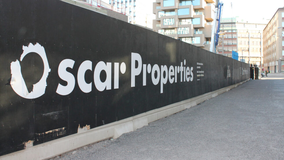 Skylt med namnet Oscar Properties och i bakgrunden skymtas de nedersta våningarna av Norra Tornen.