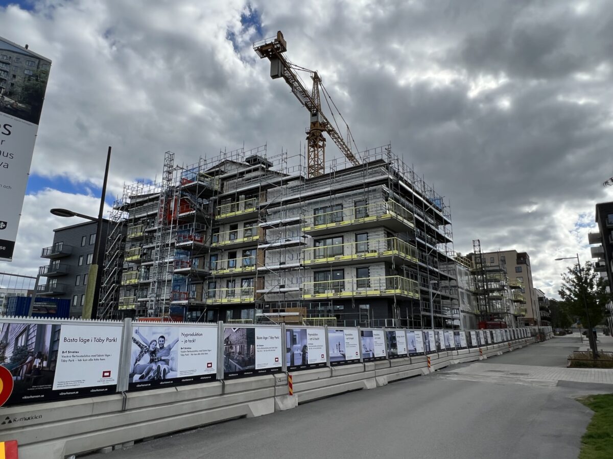 Byggarbetsplats där lägenhetsbyggande pågår. Ställningar och byggkranar på ett flerbostadshus som ännu inte är färdigbyggt.