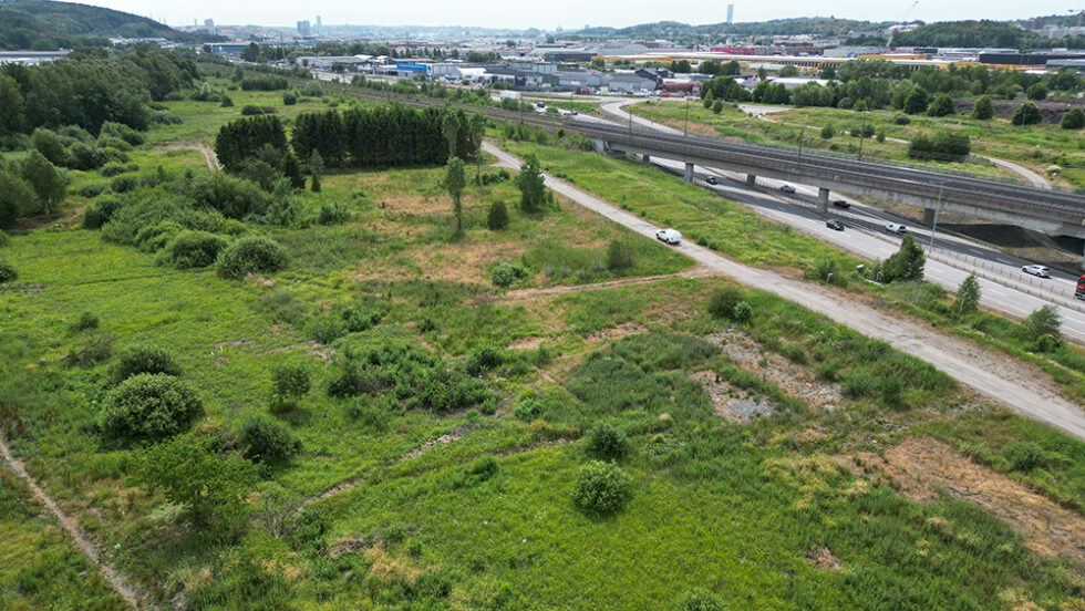 Gräsplan i förgrunden och längre bak i bilden syns trafikerad väg samt järnväg.