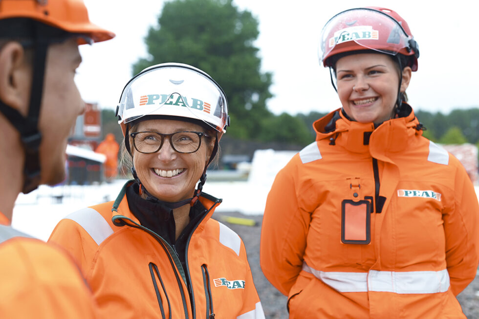 Tre personer, medarbetare från Peab, i orangea arbetskläder och bygghjälmar: två kvinnor och en man som syns i profil.