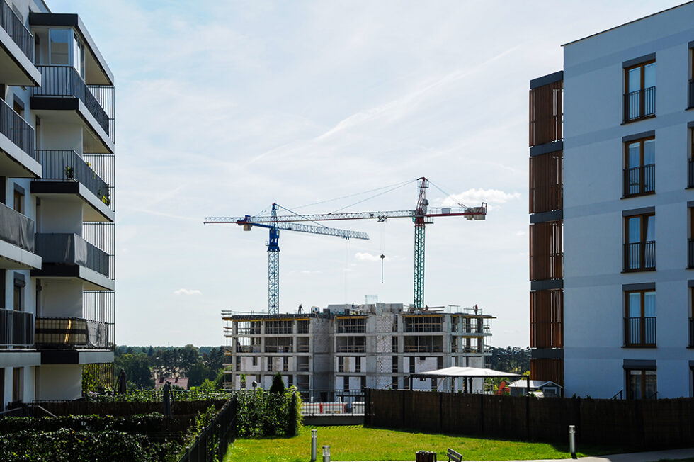 Bostadsområde med vita flervåningshus. I mitten av bilden, mellan två av husen, håller ett hus på att byggas.