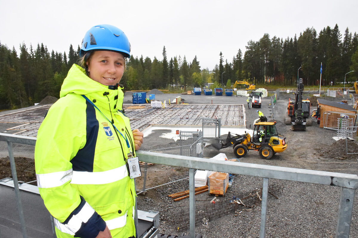 kvinna i bygghjälm och varselkläder vid en byggarbetsplats där markarbeten pågår