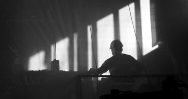 svartvit bild som visar en siluett av byggnadsarbetare i hjälm