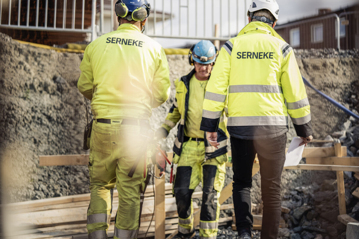 Två personer klädda i gula varselkläder, med serneke tryckt på ryggen.