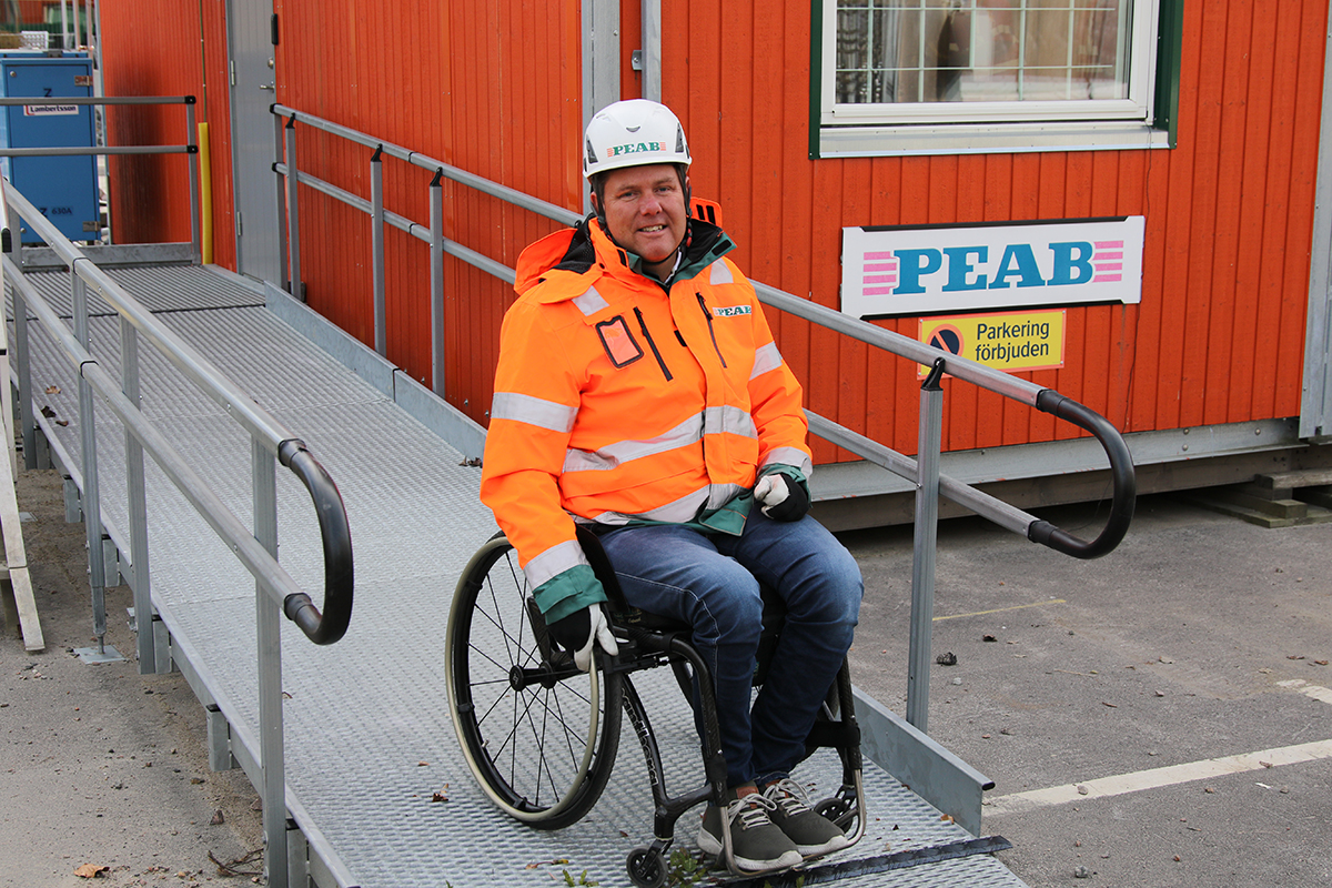 Man i varseljacka och bygghjälm som sitter i en rullstol på en ramp in i Perabs byggbodar. Peter Lindstedt, regionchef Peab Syd, är först ut I Peabs nya podd säkerhet i byggbranschen.