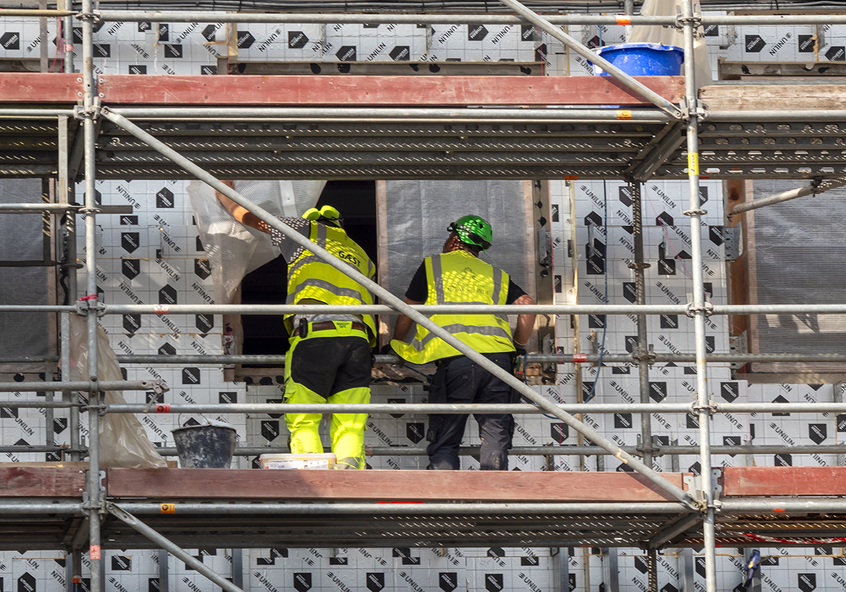 byggnadsarbetare i hjälm och varselkläder som jobbar från en byggställning, nya byggavtalet påverkar cirka 100 000 yrkesarbetare